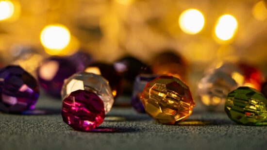 Close up of colorful faceted beads on a textured surface with golden bokeh lights in the background.