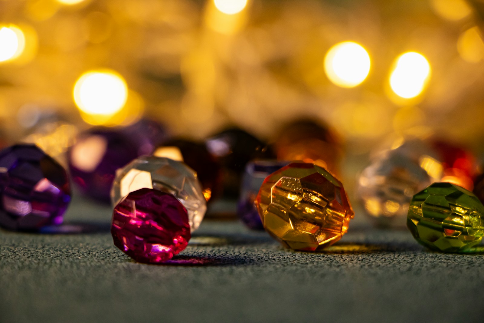 Close up of colorful faceted beads on a textured surface with golden bokeh lights in the background.